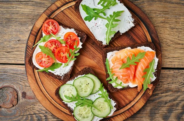 Smorrebrod - traditional Danish sandwiches. Black rye bread with salmon, cream cheese, cucumber, tomatoes on dark brown wooden background