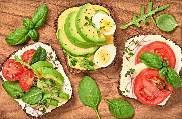 Open sandwiches with avocado, tomato, mozzarella and soft cheese. Homemade sandwich with cherry tomato, boiled egg, radish sprouts on wooden board. Top view, sandwich closeup