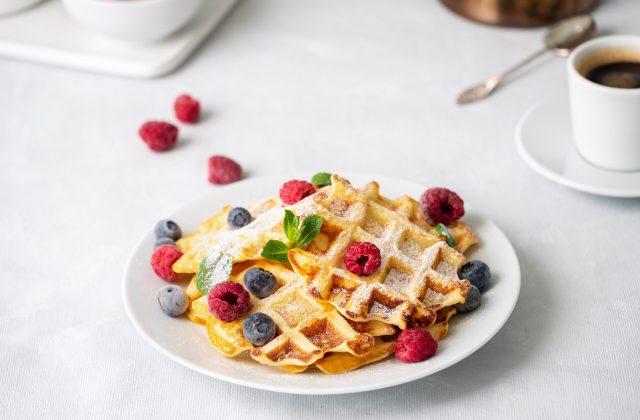 Belgian waffles with raspberries, blueberries, curd and coffee, side view. Healthy homemade breakfast, light concrete background