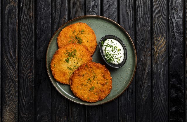 Potato pancakes with sour cream sauce garnished with dill, served on a green plate on rustic wooden backdrop, top view